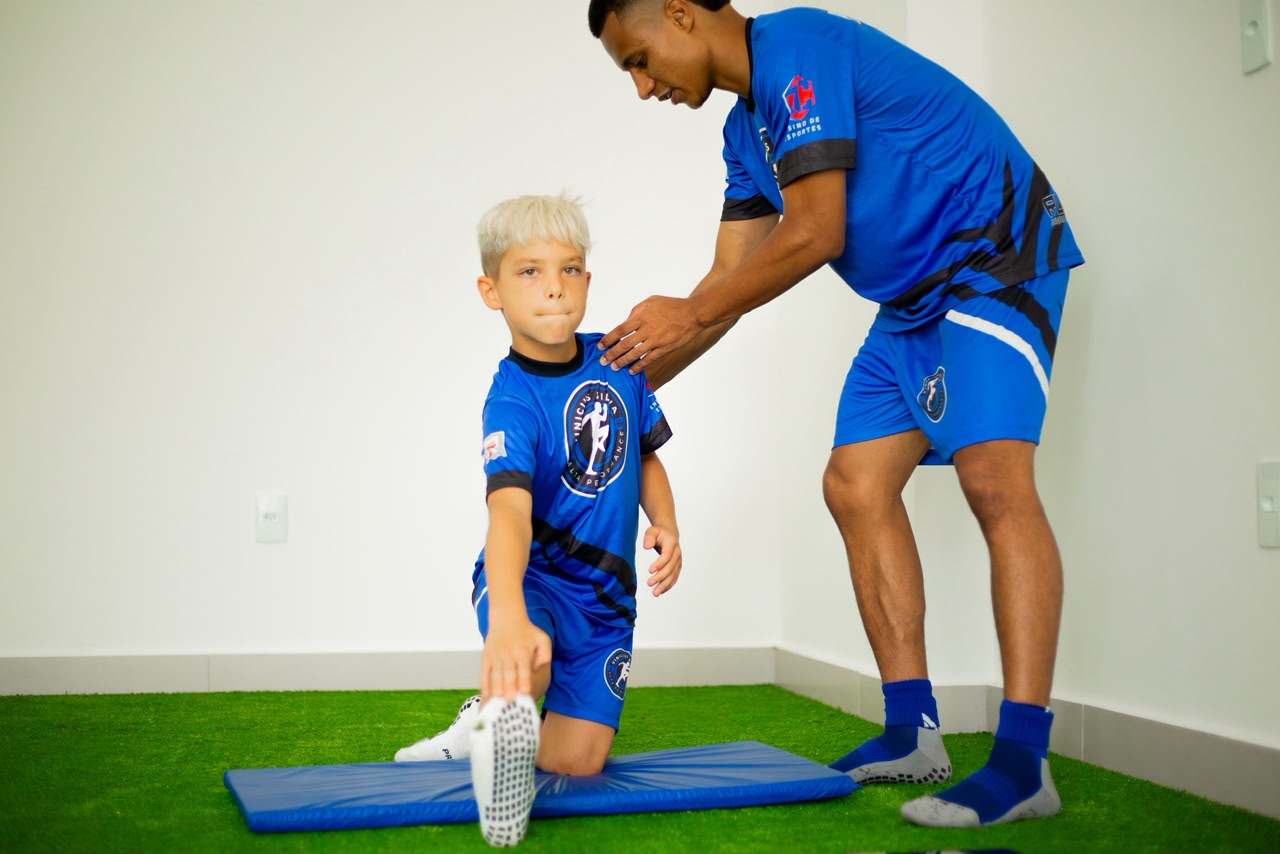 Treinador orientando alongamento de aluno no gramado sintético